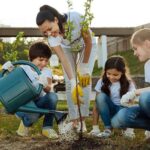 Woman helping group of children plant a tree