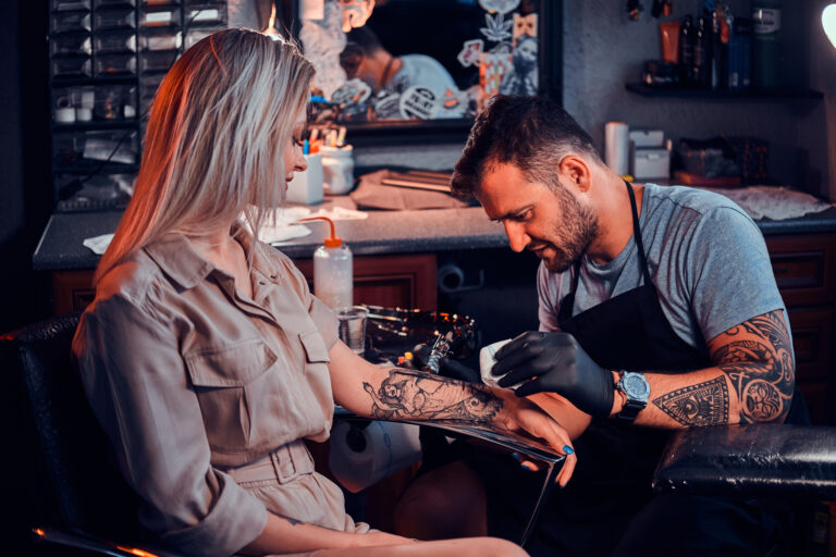 Tattooist working on design on a woman's arm.