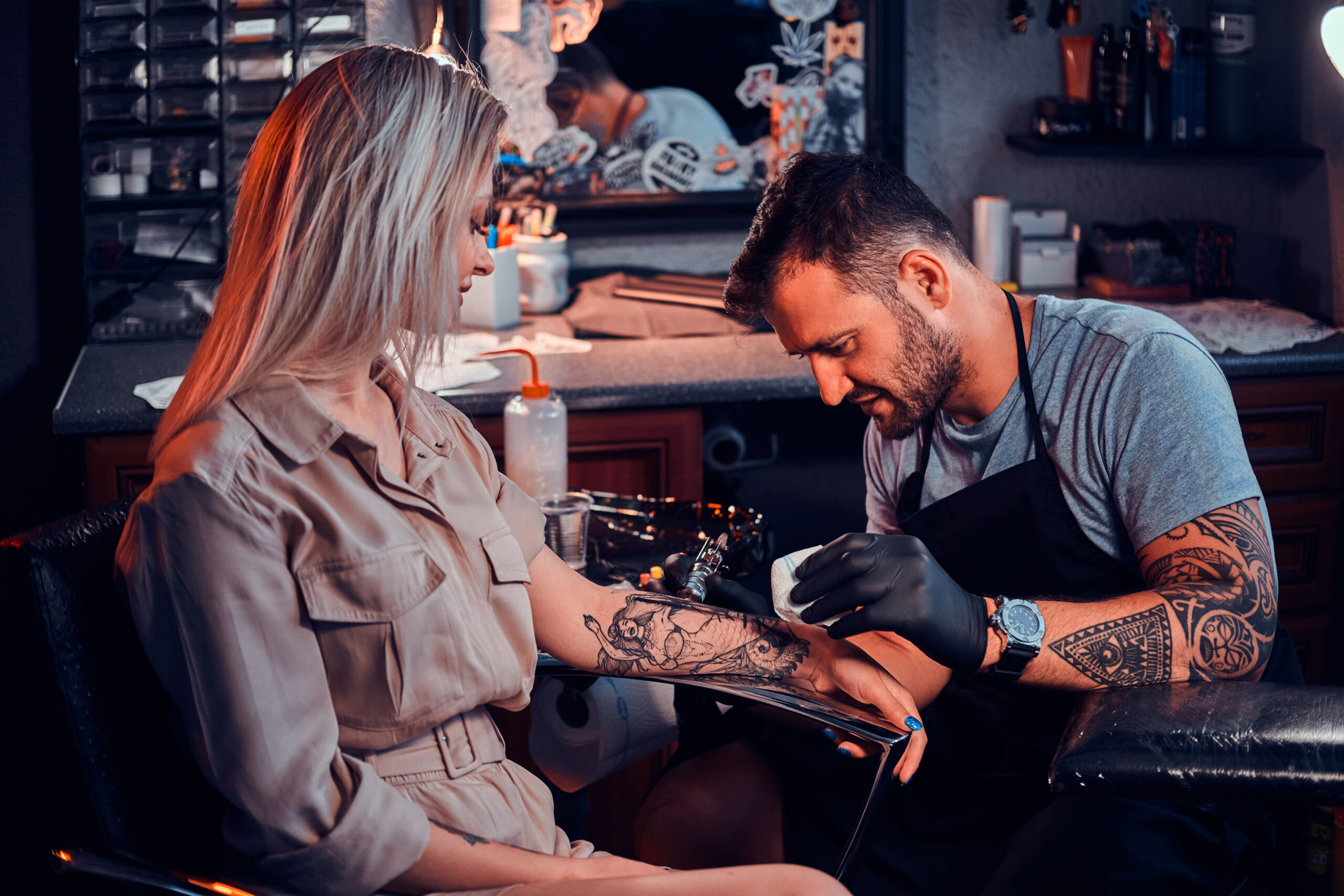 Tattooist working on design on a woman's arm.