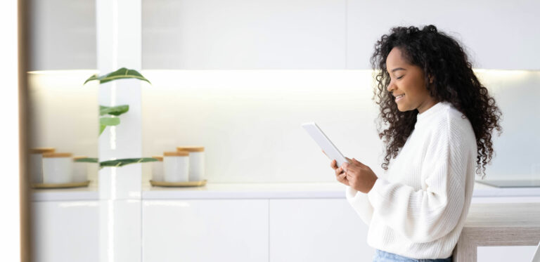 Woman smiling and looking at a tablet in her kitchen.